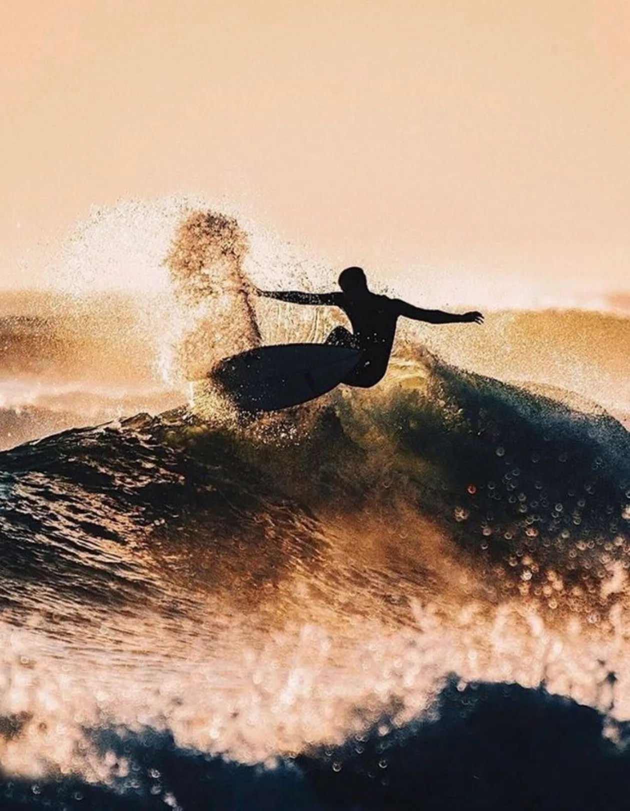 Surfer carving across a wave at sunset